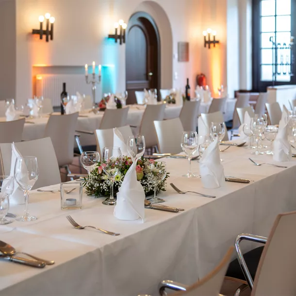 A long table set with a white tablecloth, glasses, cutlery, napkins, etc.